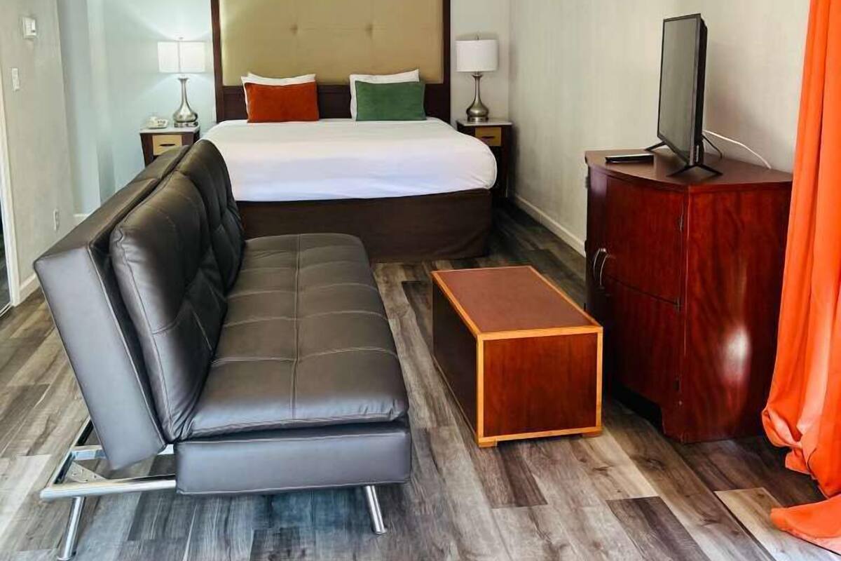 A hotel room with a large bed, a leather sofa, a wooden side table, and a TV.