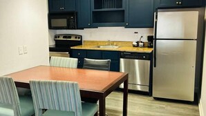 A compact kitchen with dark blue cabinets, a stainless steel refrigerator, a microwave, and a dishwasher. - Extended Stay of Charleston (North Charleston)