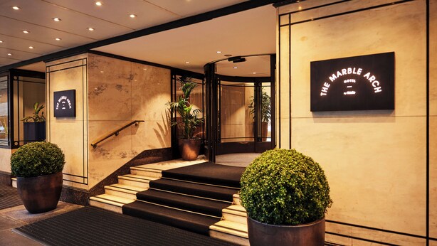 Un vestíbulo de hotel con paredes de mármol, una escalera y plantas en macetas.