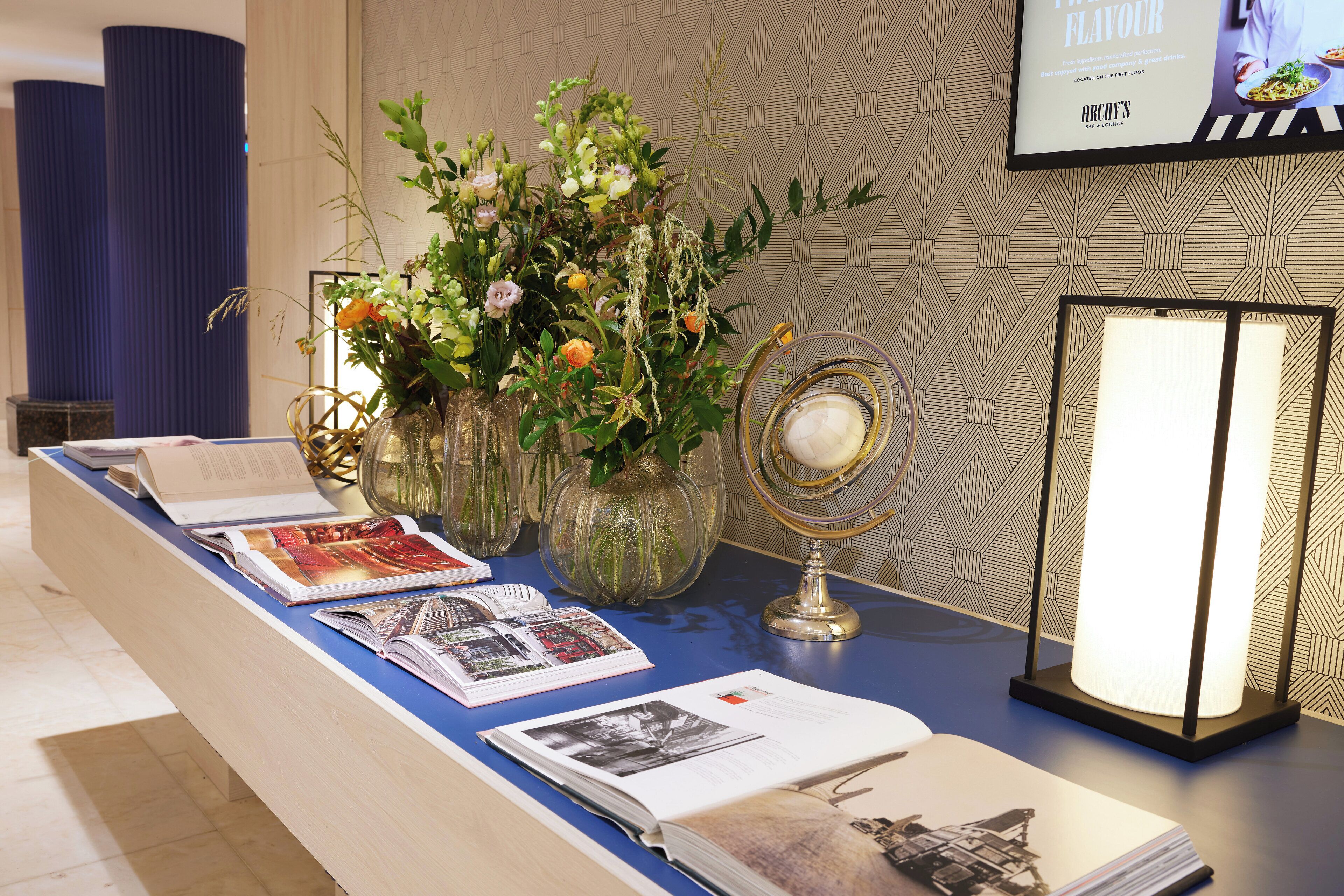 A reception desk with brochures, a vase with flowers, a lamp, and a framed menu on the wall.