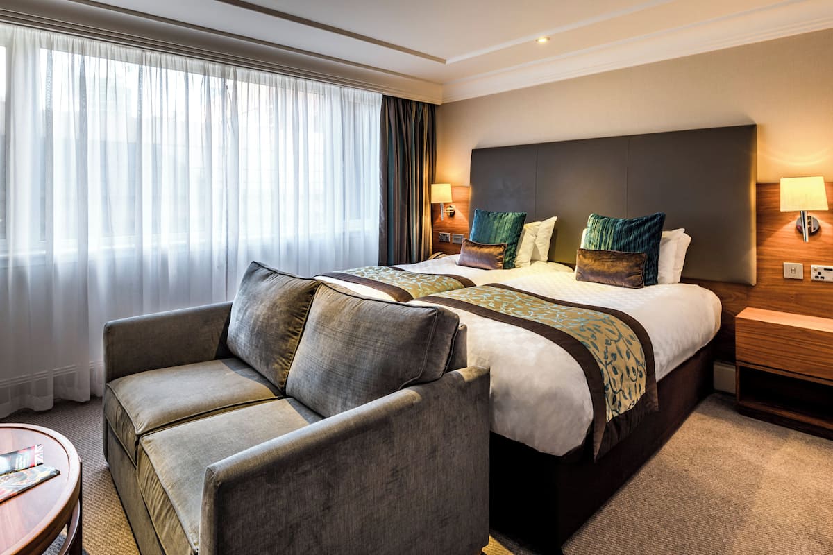 A hotel room with a large bed, two bedside tables, a sofa, and a small table.