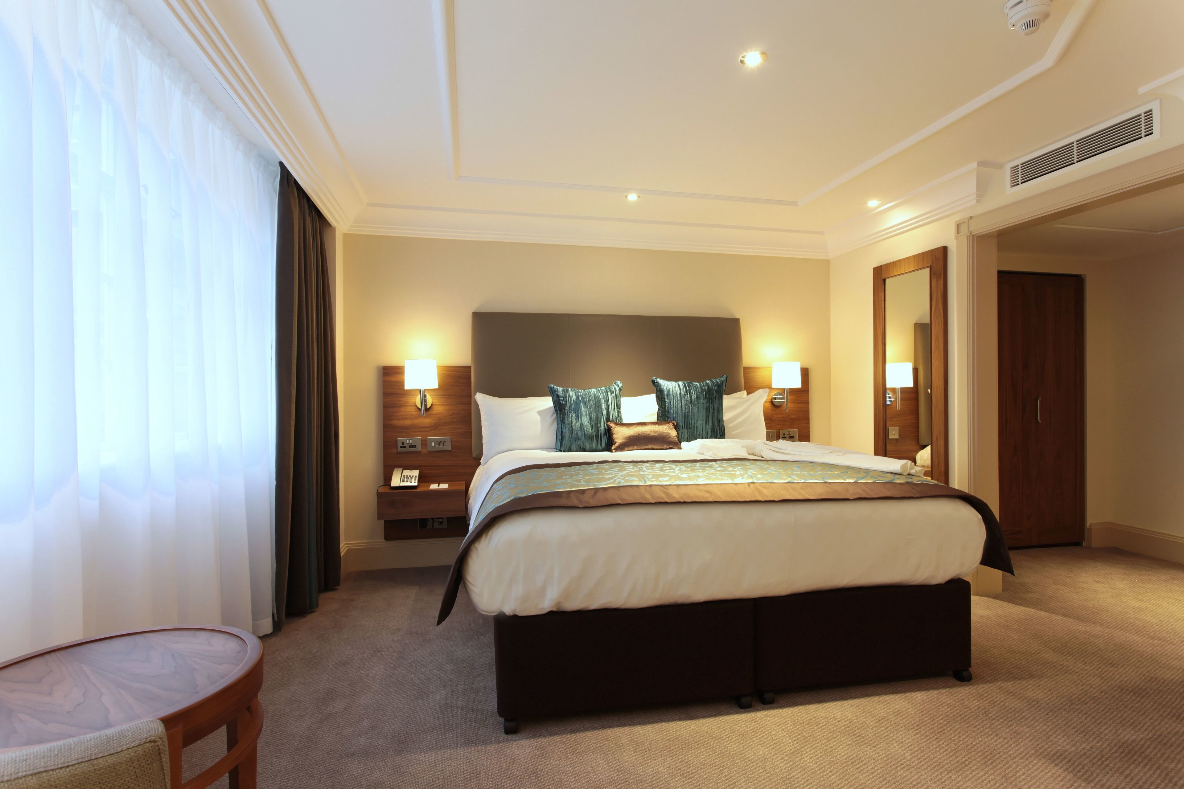 A hotel room with a large bed, bedside tables with lamps, a wooden headboard, and a view of the hallway.
