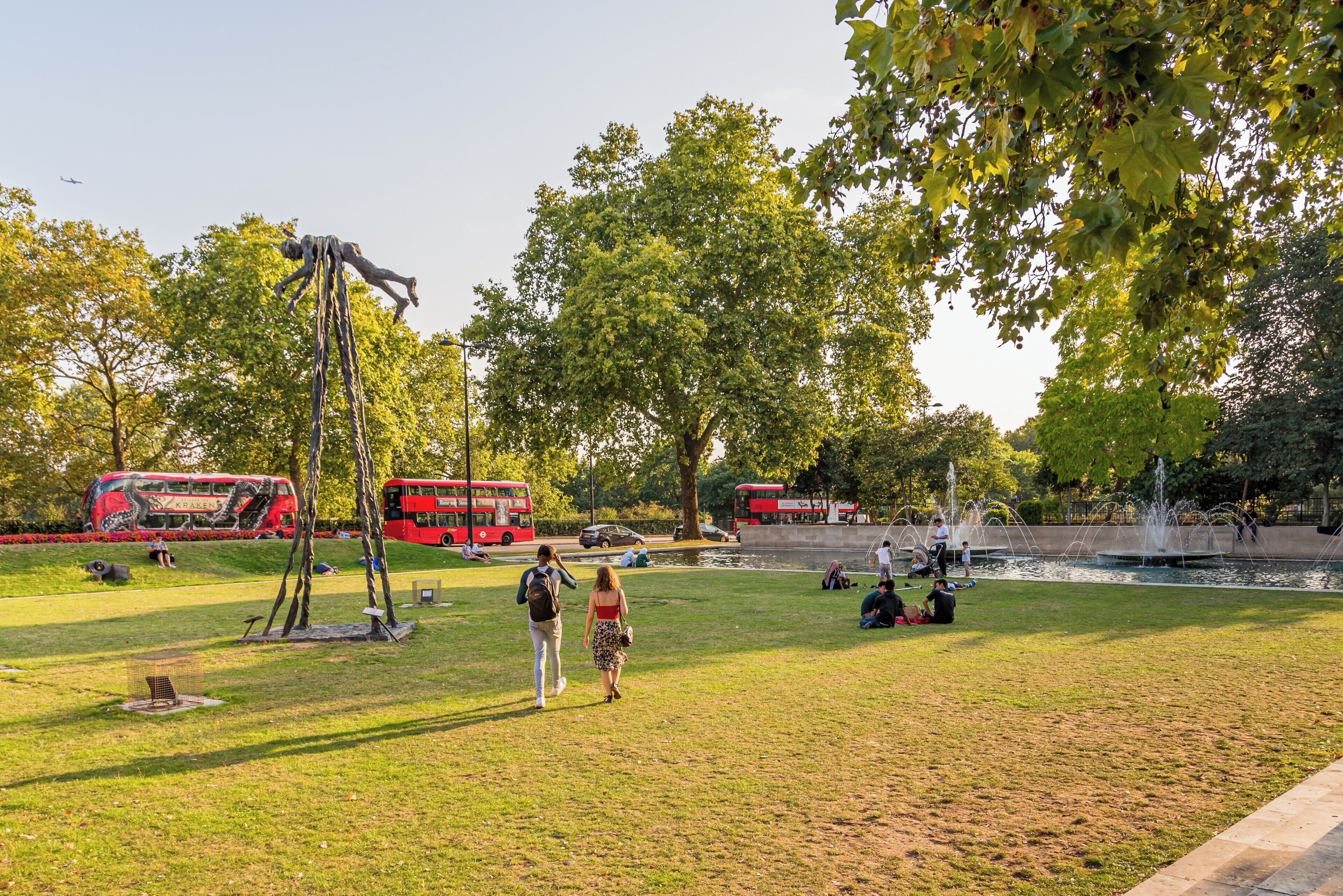 En park med røde turistbusser, en skulptur og en springvand.