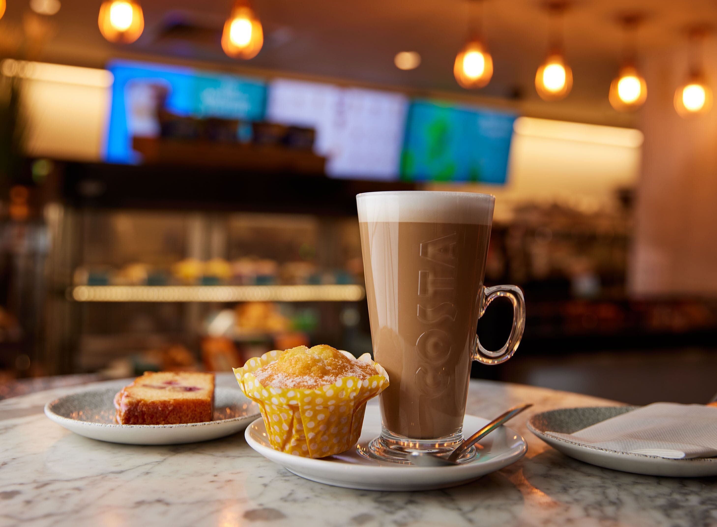 A coffee cup and a muffin on a table with a spoon.