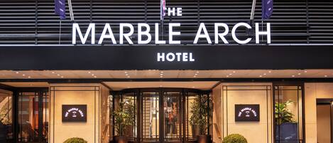 The Marble Arch Hotel entrance with a black facade, large glass doors, and potted plants.