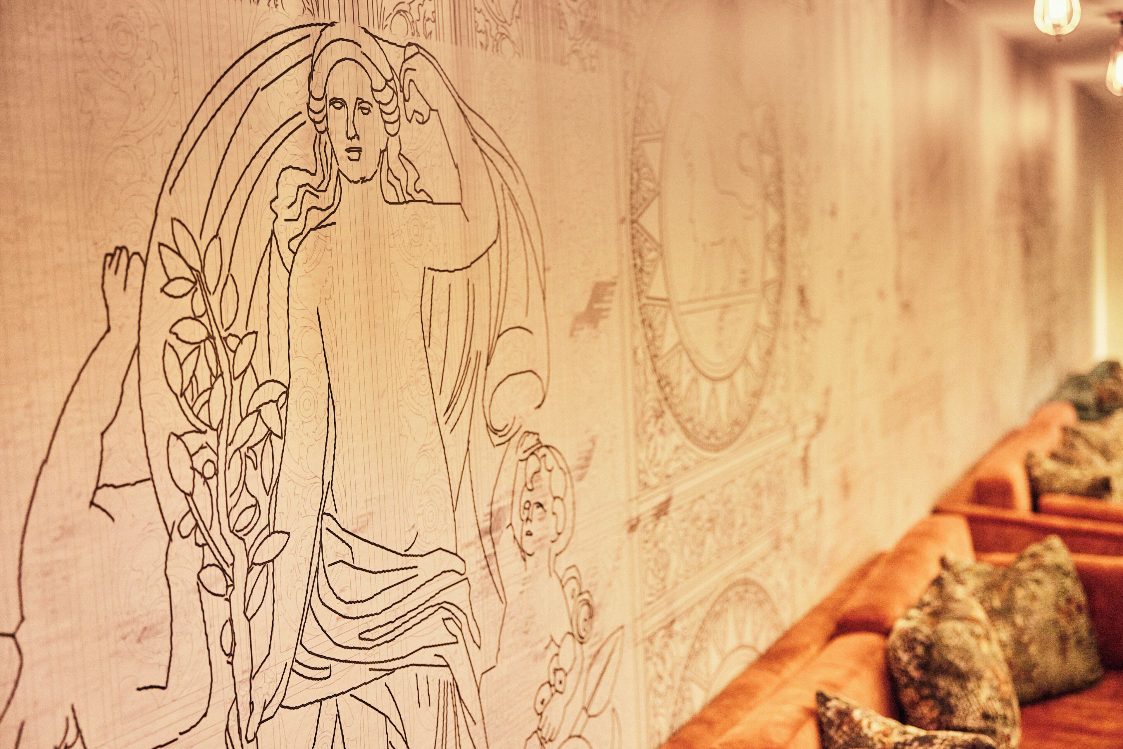 A detailed line drawing of a classical figure on a wall, with a sofa and decorative pillows in the foreground.