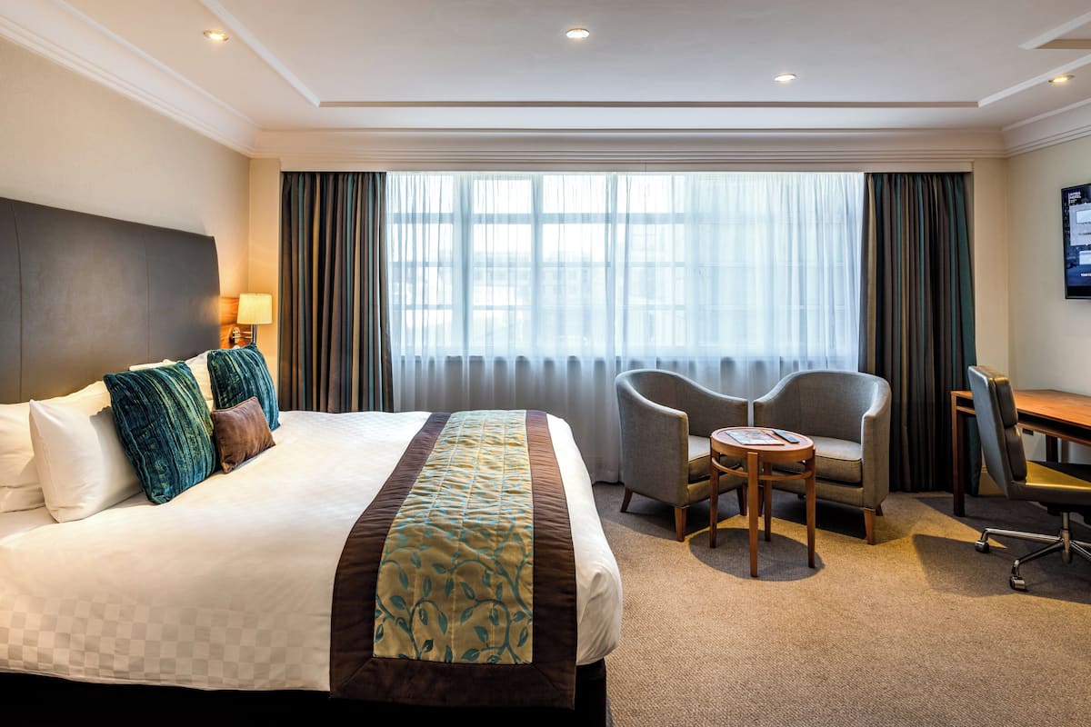 A hotel room with a large bed, two armchairs, a small table, and a desk.