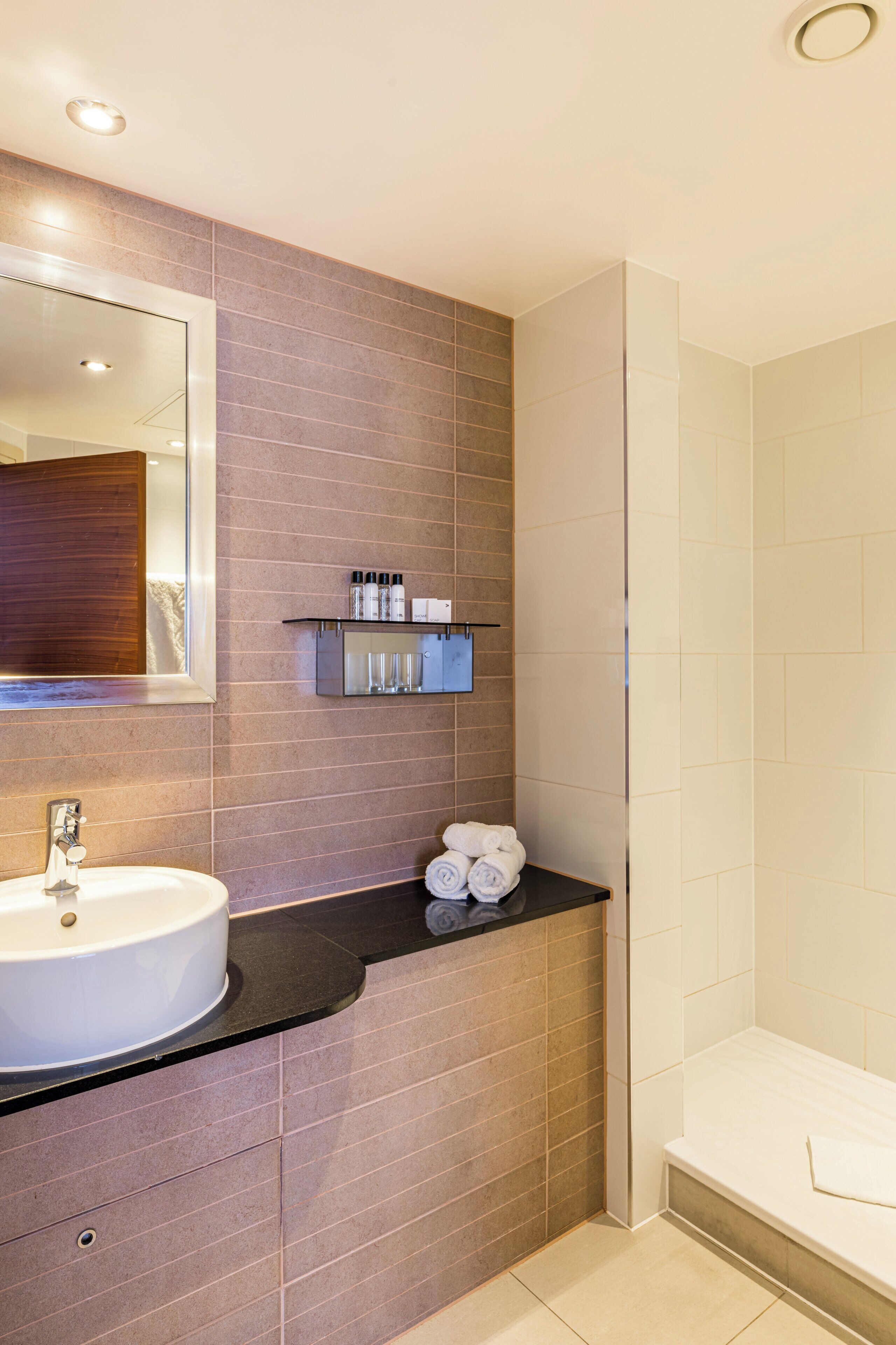 Un baño con lavamanos, espejo, toallero y zona de ducha.