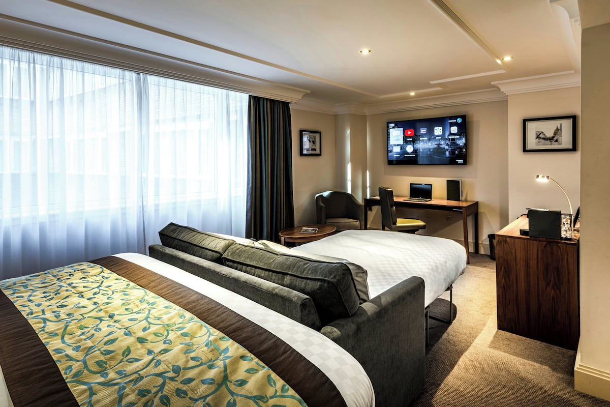 A hotel room with a large bed, a desk, a chair, a TV, and a window with curtains.
