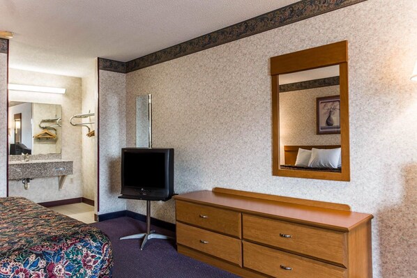 A hotel room with a bed, a dresser, a television, a mirror, and a bathroom with a sink and towel rack. - Rodeway Inn University Area (Charlotte)