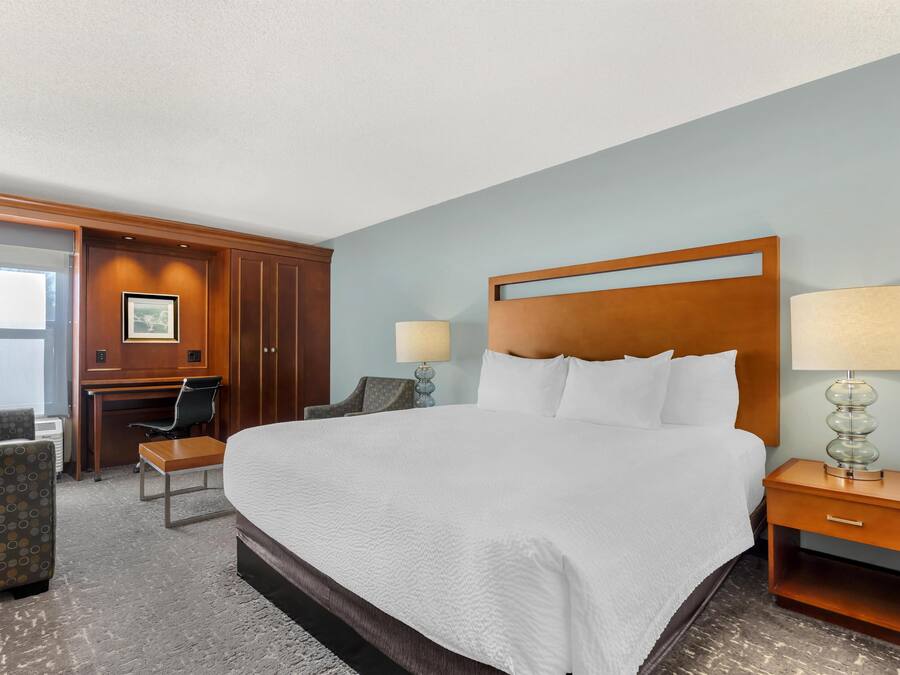 A hotel room with a large bed, two bedside tables with lamps, a desk with a chair, and a small seating area.