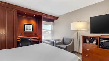 A hotel room with a large bed, a desk, a chair, a TV, a lamp, and a coffee machine.