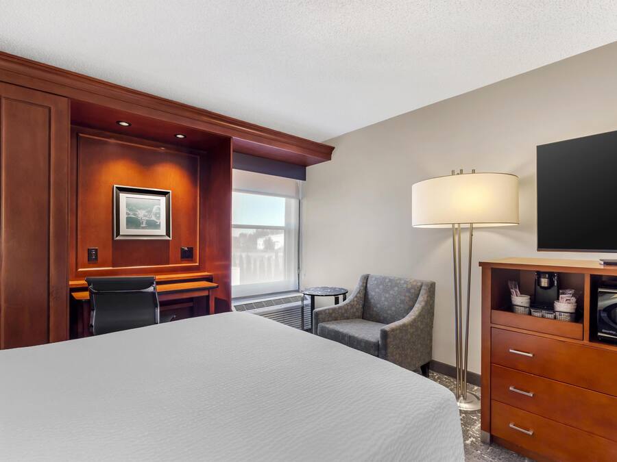 A hotel room with a large bed, a desk, a chair, a TV, a lamp, and a coffee machine.