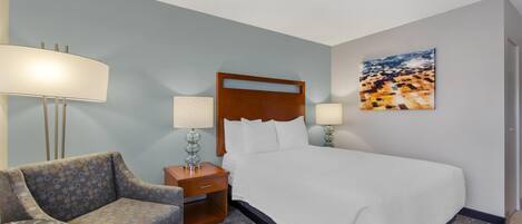 A hotel room with a large bed, a sofa, a small table, and two bedside lamps.