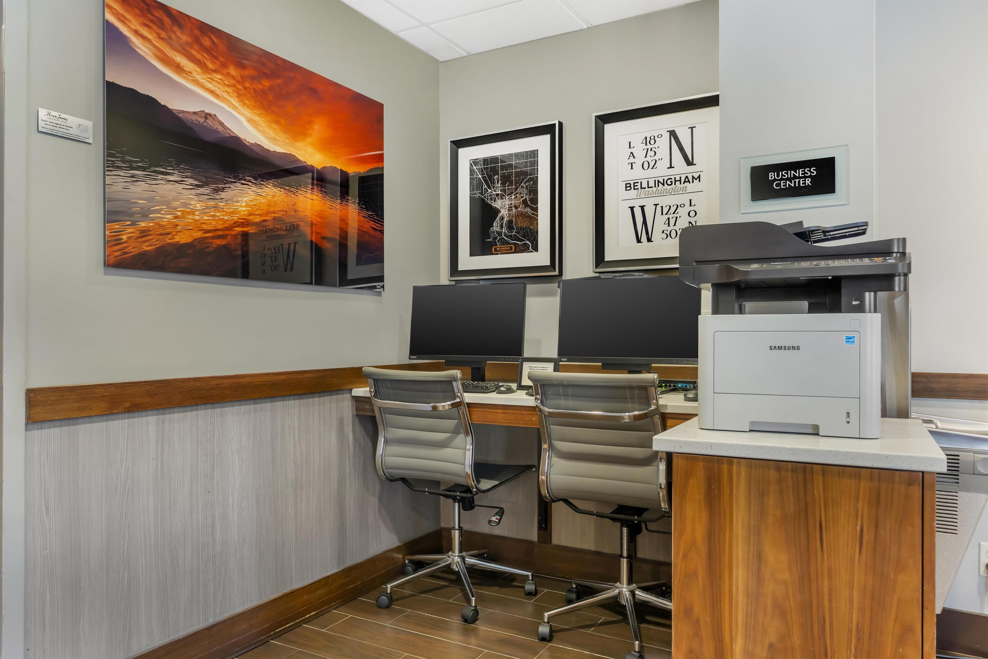 A modern office with two desks, chairs, and a large painting of a sunset over a lake.