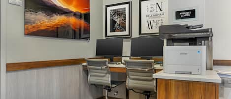 A modern office with two desks, chairs, and a large painting of a sunset over a lake.