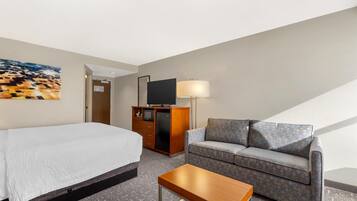 Una habitación de hotel con una cama, un sofá, un televisor sobre un mueble de madera, una lámpara y un cuadro en la pared.