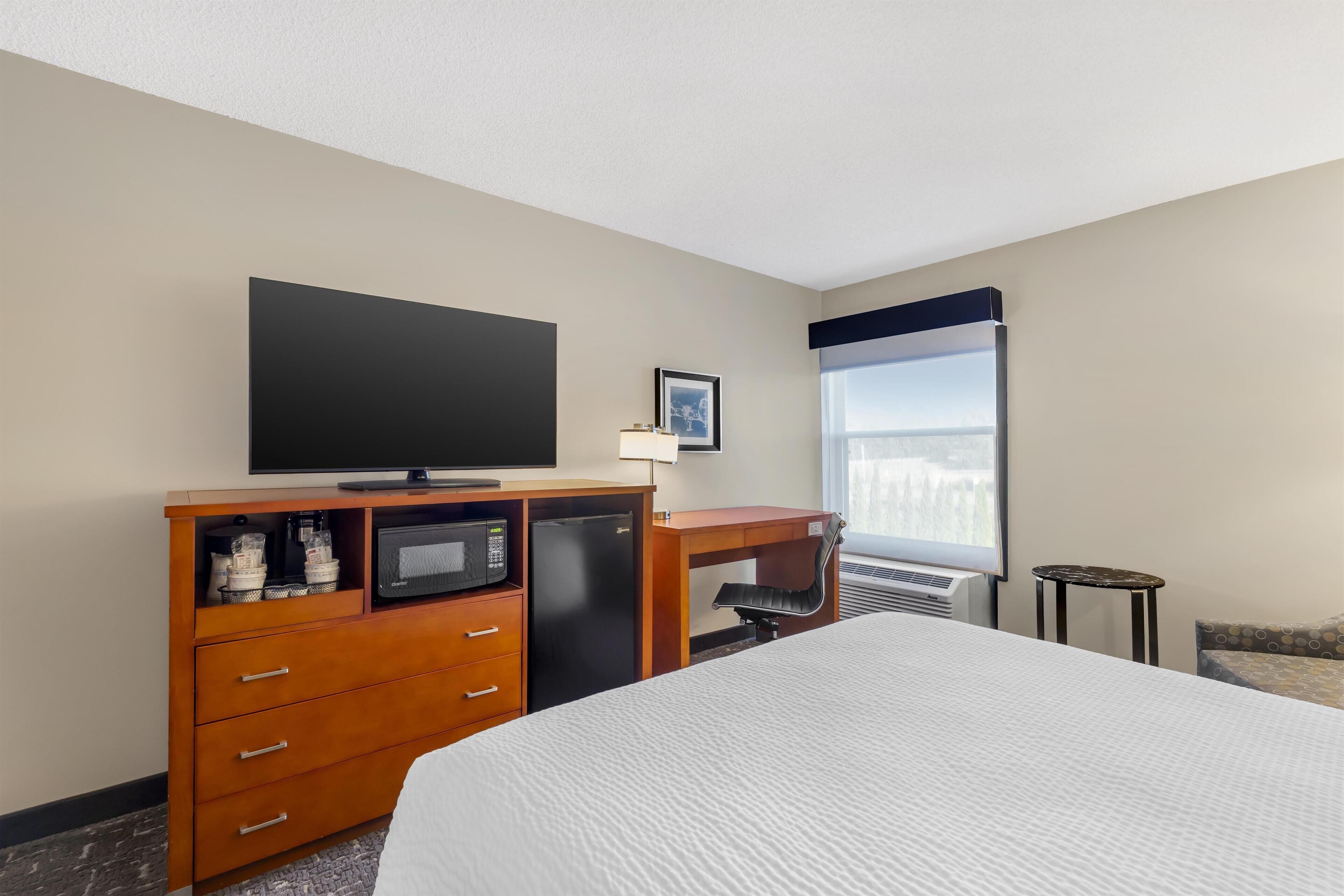 Habitación de hotel con una cama, un escritorio con computadora, televisor, microondas y una mesita.