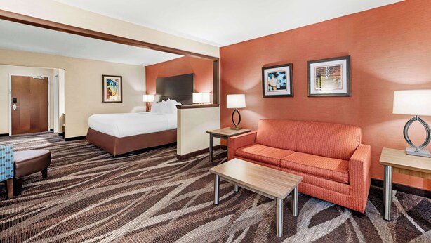 A hotel room with a bed, a sofa, a coffee table, a desk, and two lamps. - Best Western Maple City Inn (Hornell)