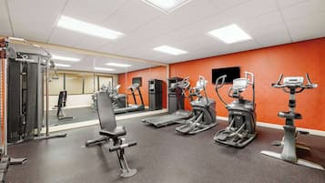 Een sportschool met diverse fitnessapparaten, een spiegel en oranje wanden.