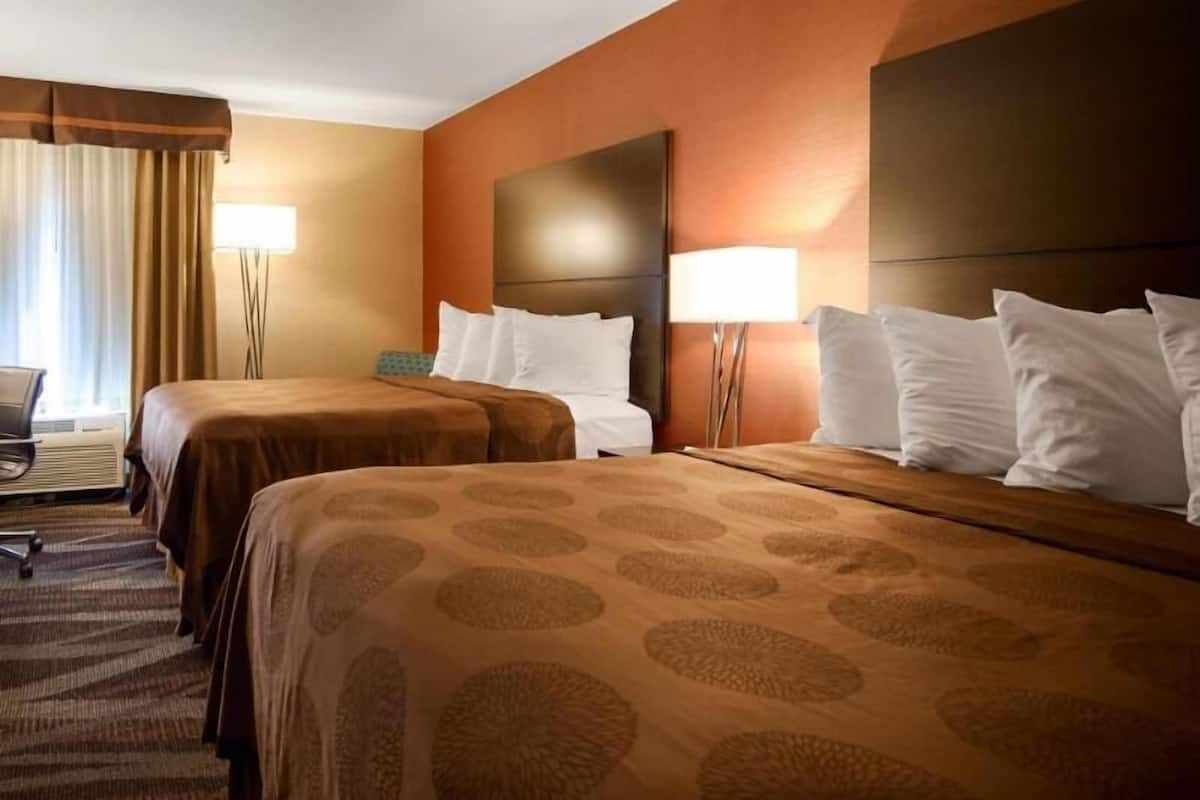 A hotel room with two beds, a desk, and a chair.