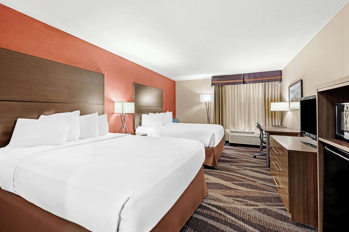 A hotel room with two beds, a desk, a TV, and a large window with curtains.