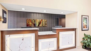 A reception area with marble countertops, a dark wall with a colorful abstract painting, and a potted plant. - Best Western Maple City Inn (Hornell)