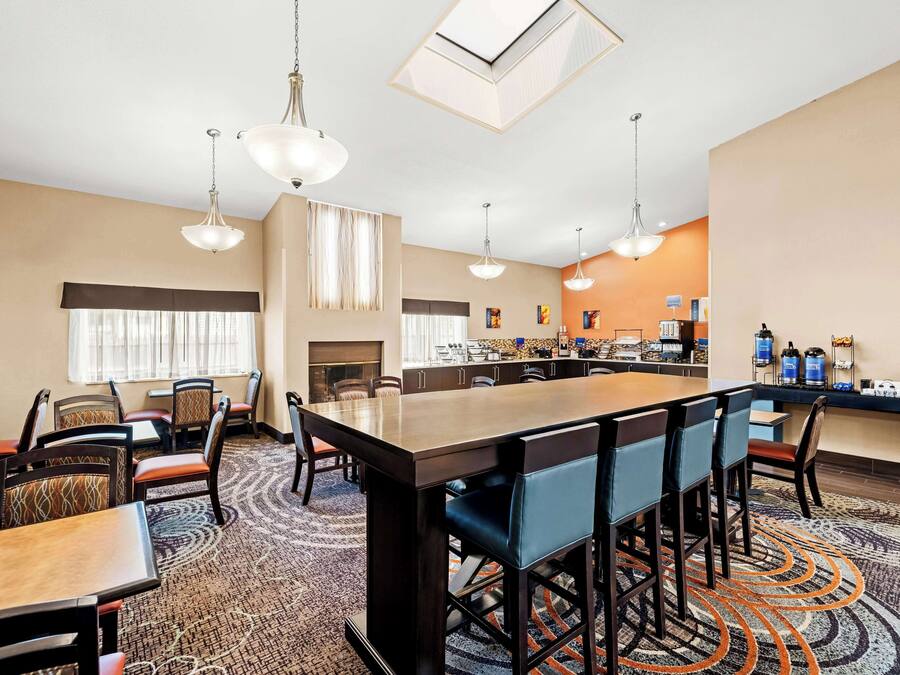 Un'area ristorazione di un hotel con un lungo tavolo condiviso, diverse sedie e un angolo cottura sullo sfondo.