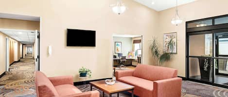 A hotel lobby with a carpeted floor, a sofa, a coffee table, and a television on the wall.