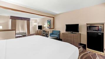 Een hotelkamer met een groot bed, een bureau met stoel, een televisie, een magnetron en een koelkast.