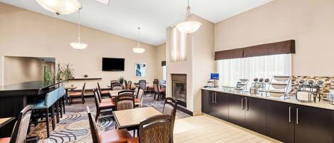 A hotel room with a dining area, a fireplace, and a kitchenette.