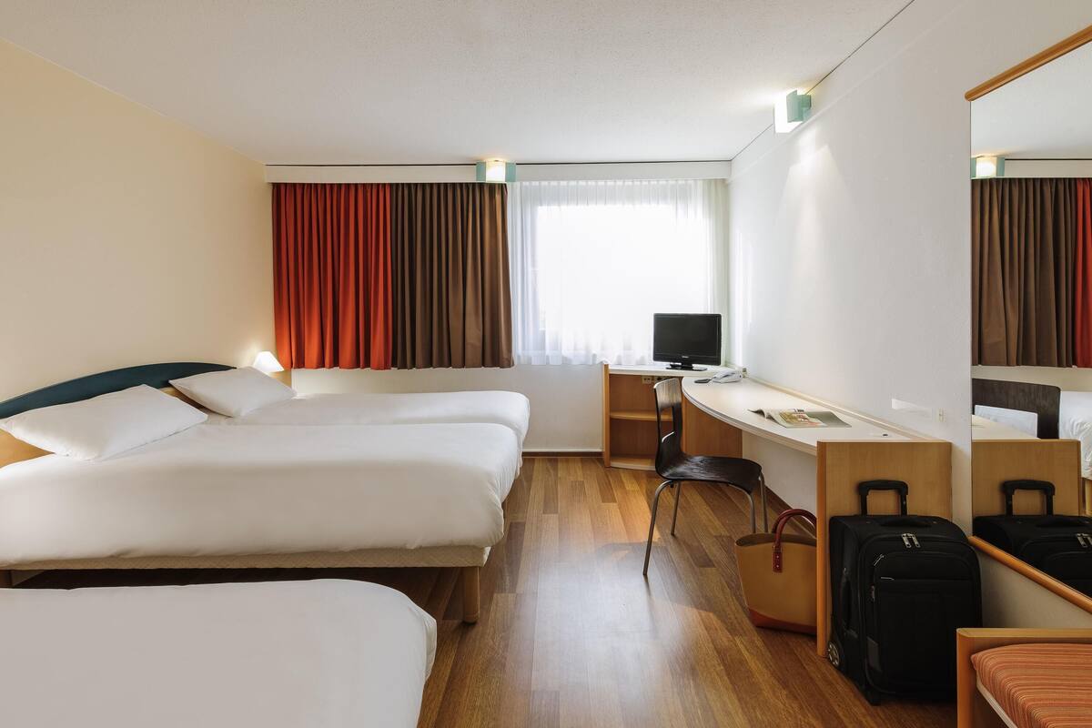 A hotel room with three beds, a desk with a computer, a chair, and a mirror.