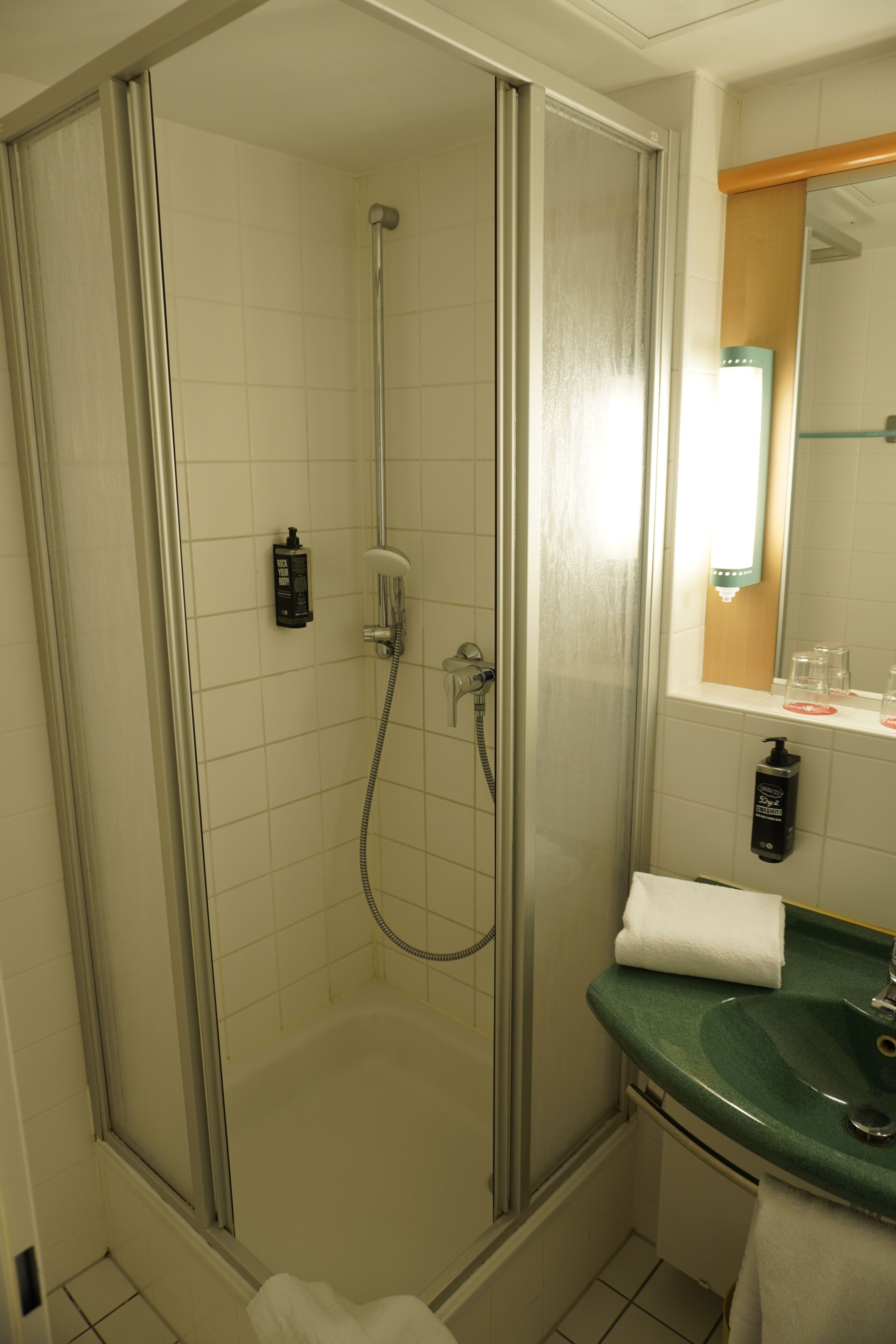 A shower with a glass door, a sink with a green countertop, and a mirror above the sink.