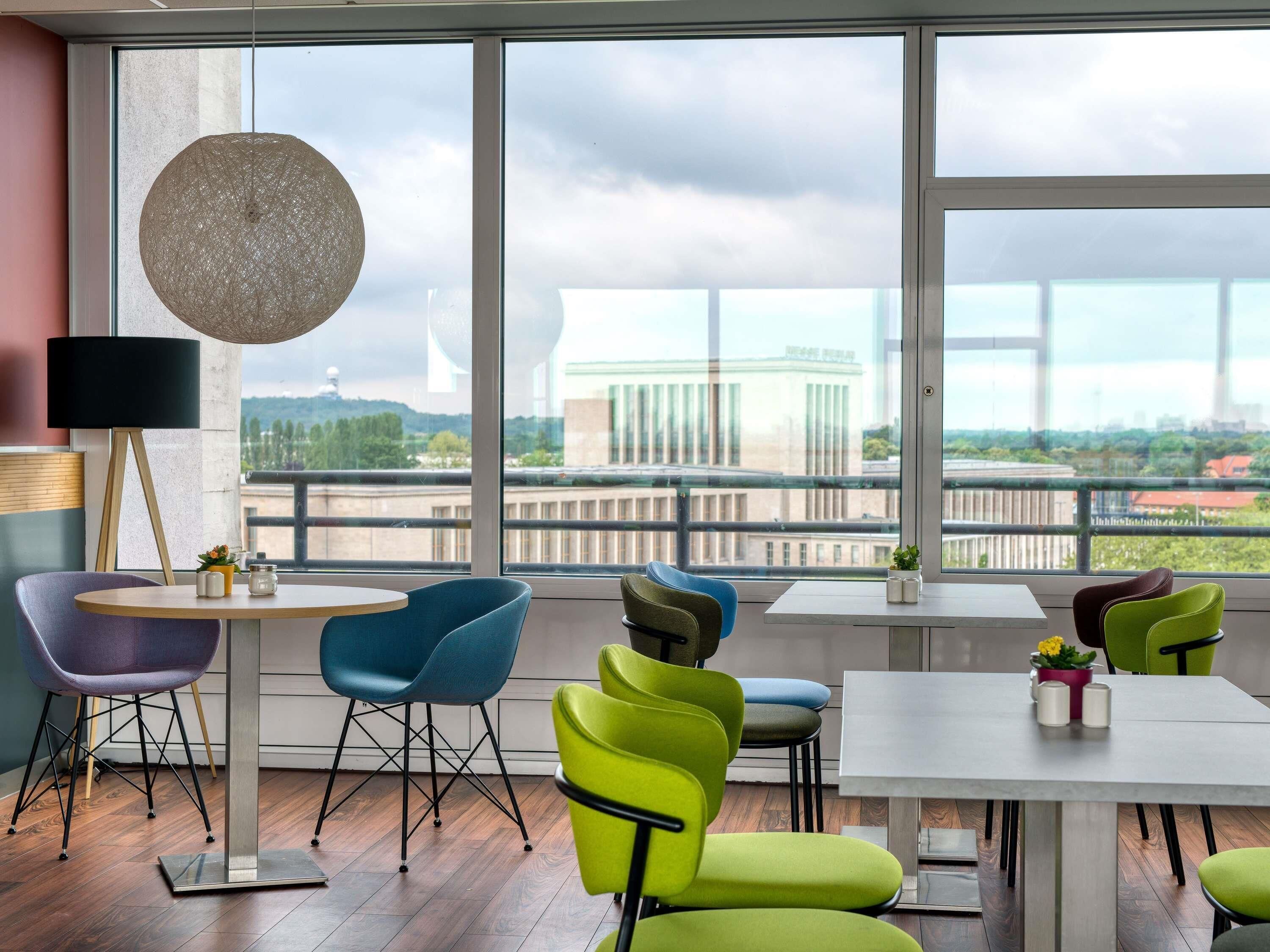 A modern dining area with a large window, a round hanging light, and colorful chairs.