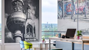 A modern office space with a large window, a desk with a laptop, and colorful chairs. - ibis Berlin Messe (Berlin)