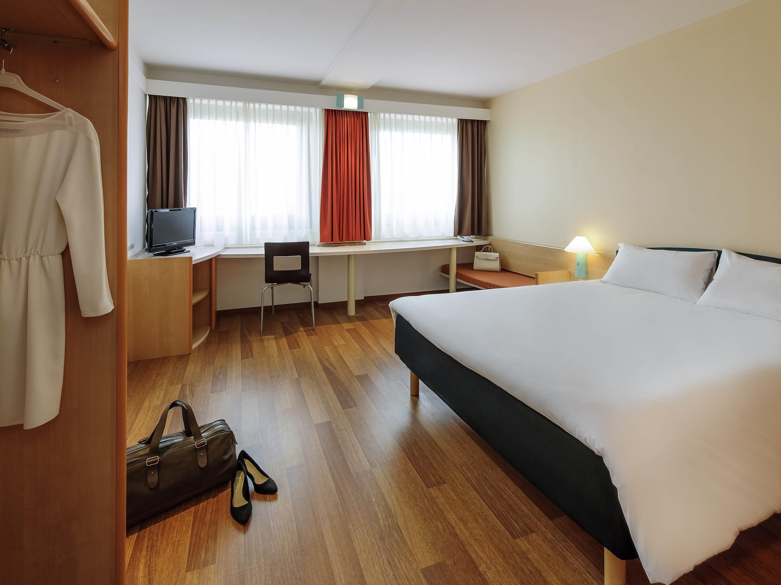 A hotel room with a bed, desk, chair, and wardrobe.