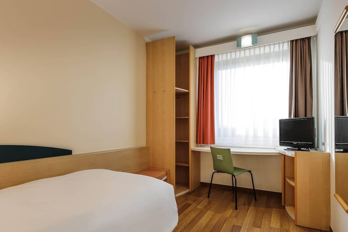 Una camera d'albergo con un letto, una scrivania con un computer, una sedia, una televisione e un armadio.