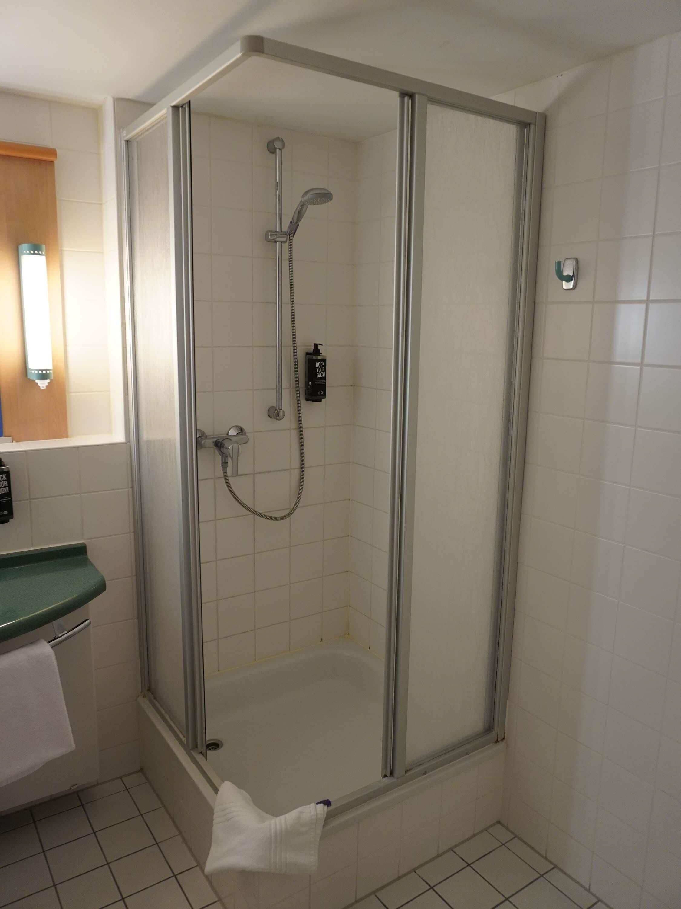 A shower with a glass door, a handheld showerhead, and a bottle of shampoo.