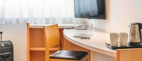 A hotel room with a desk, a chair, a television, a coffee maker, and a suitcase.