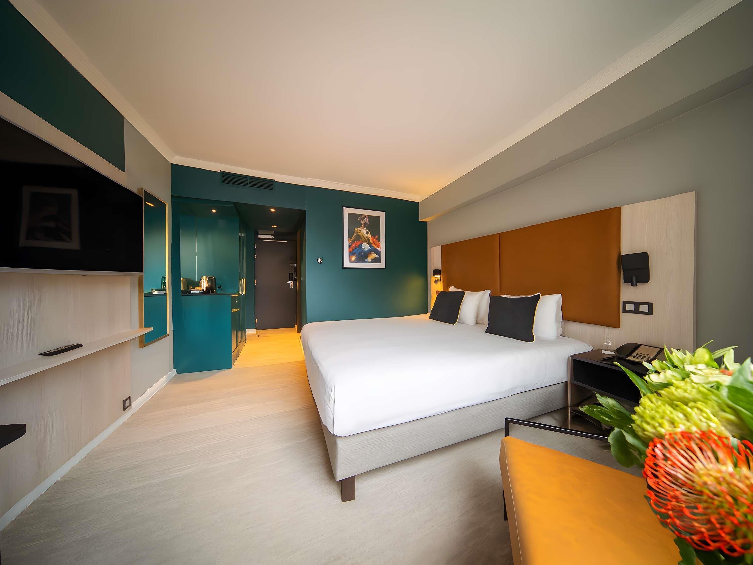 A modern hotel room with a bed, bedside table, and a desk with a chair.