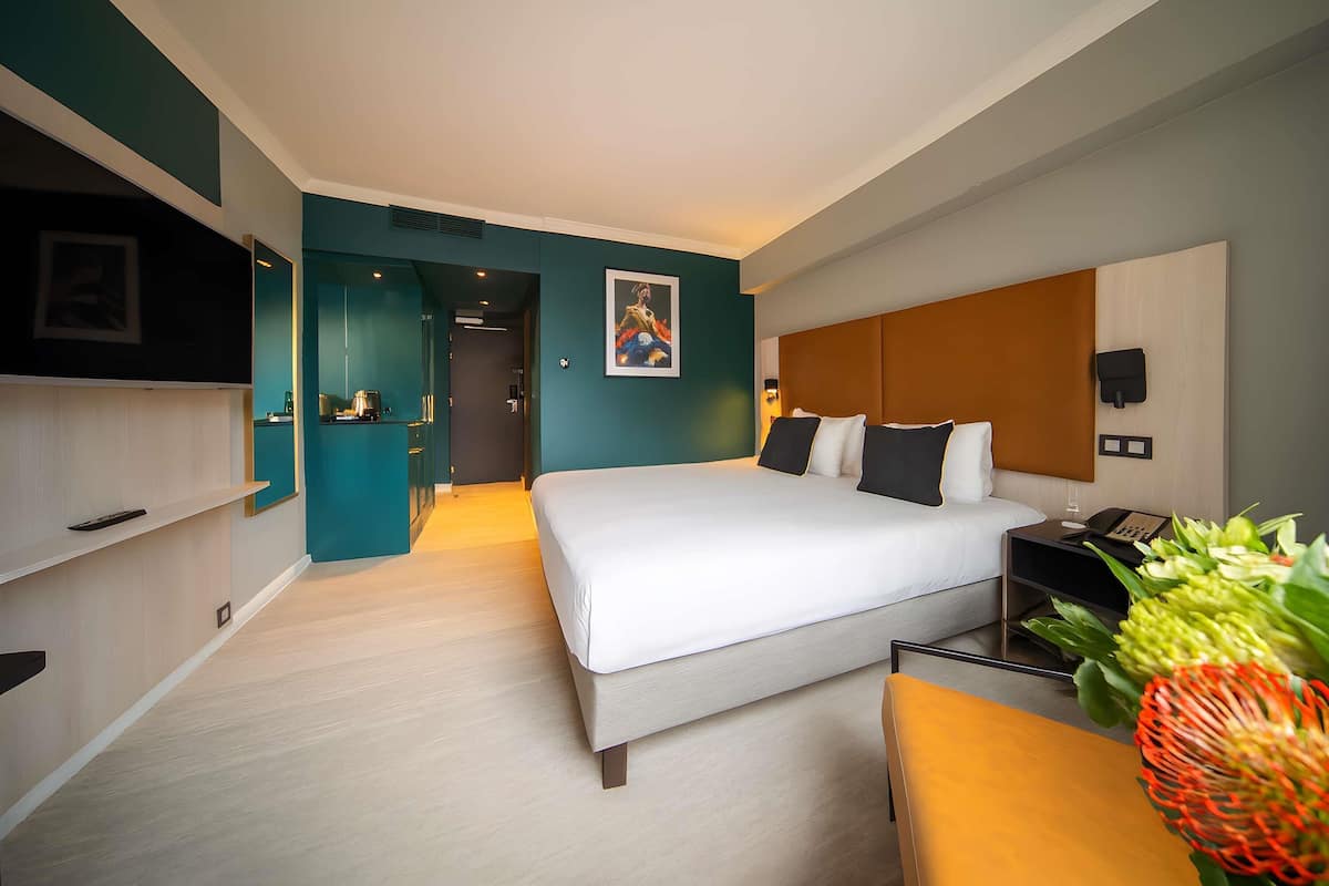 A modern hotel room with a bed, bedside table, and a desk with a chair.