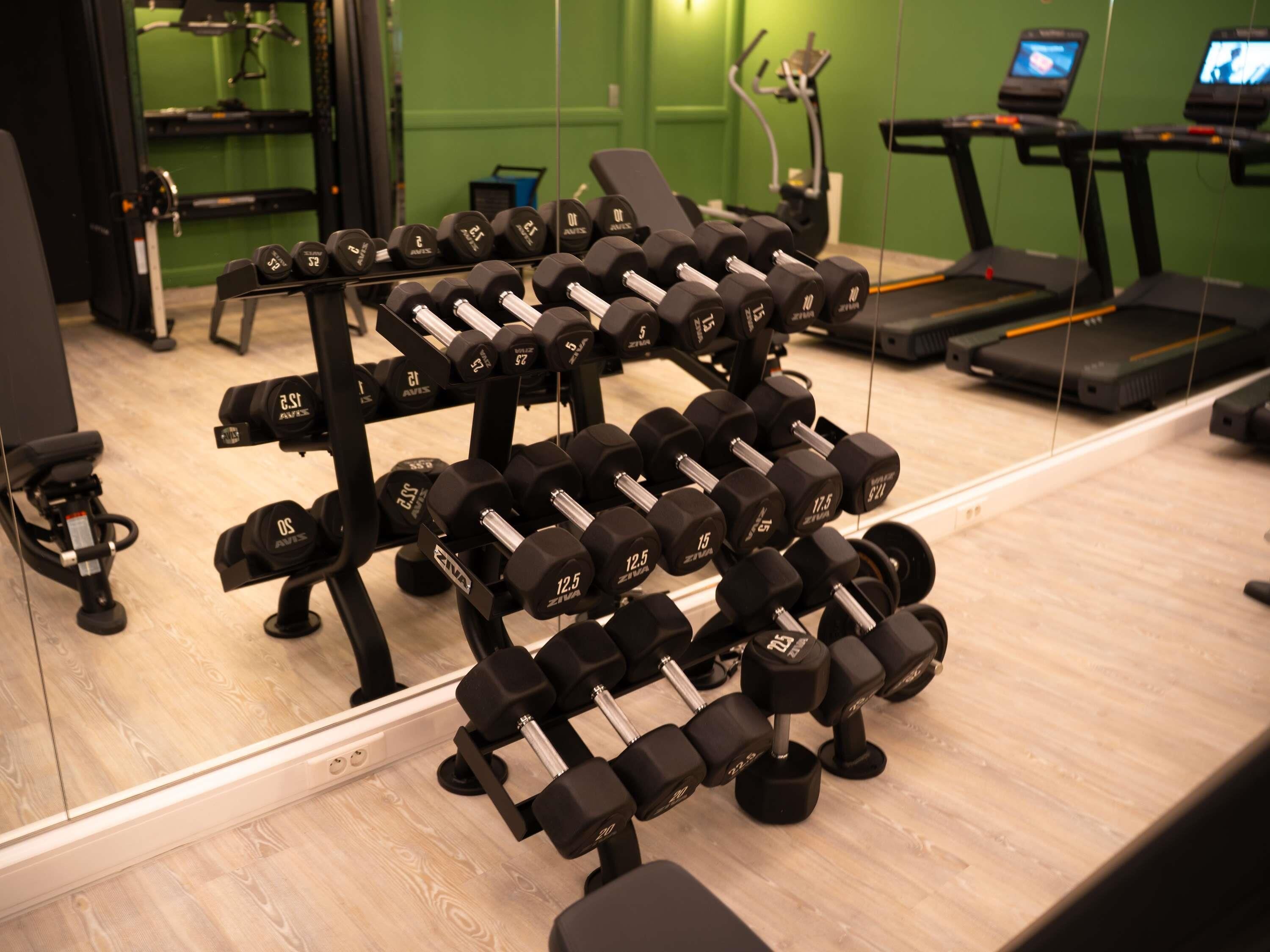 Une salle de sport dotée de miroirs qui reflètent les équipements, notamment les haltères et les tapis de course.