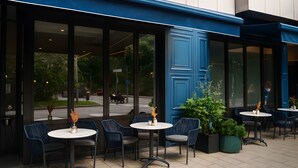 An outdoor seating area with tables and chairs, large windows, and potted plants. - Maek Hotel Antwerp Central - Handwritten Collection (Antwerp)