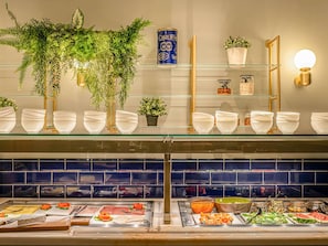 A buffet area with various food items, glass shelves with white bowls, and decorative plants.