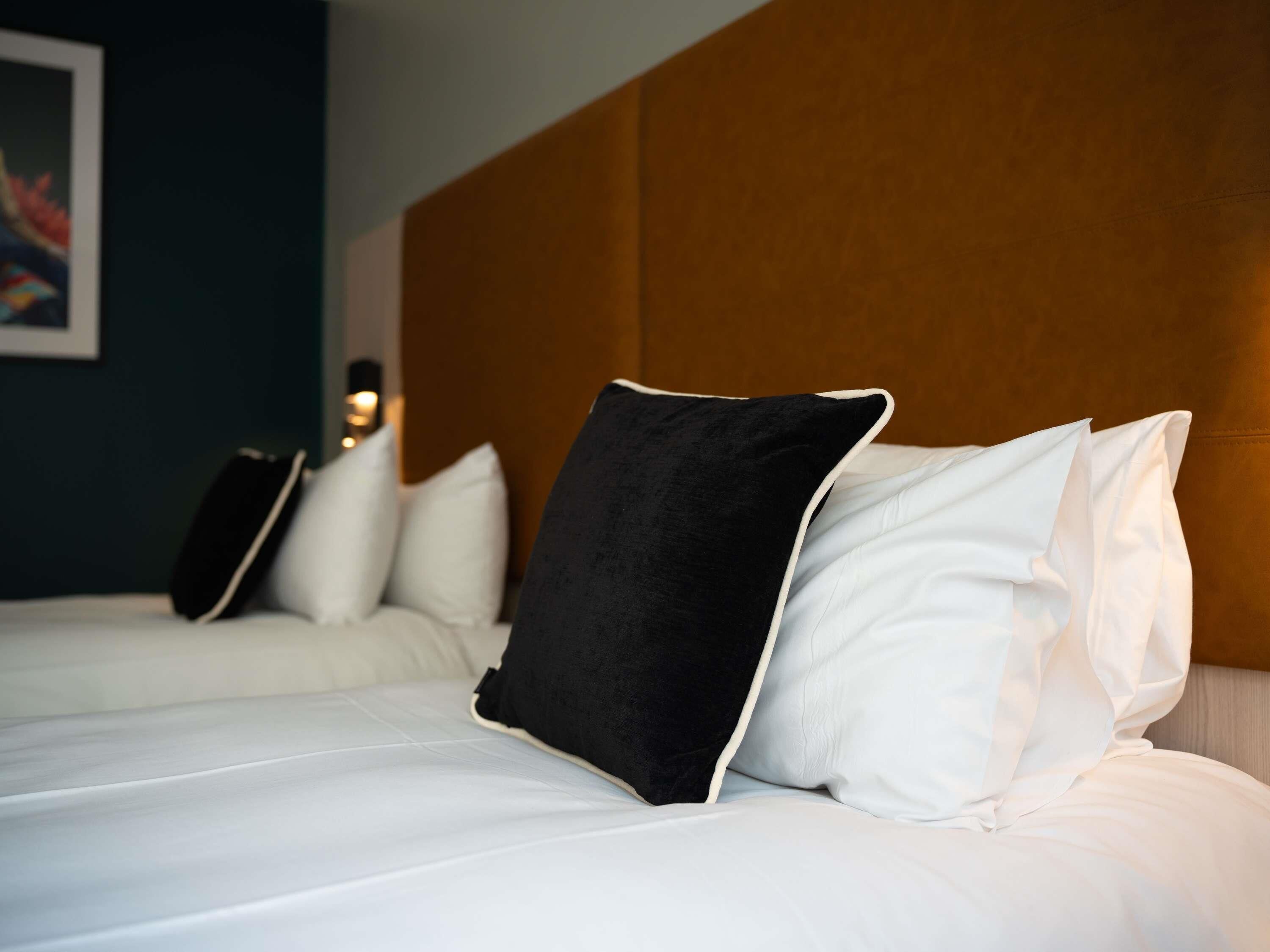 Een hotelkamer met een groot bed, witte beddengoed, een bruin hoofdeinde en een schilderij aan de muur.