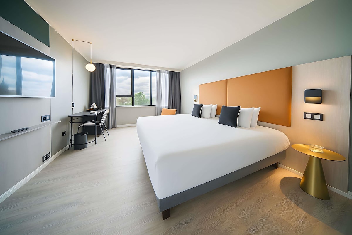 A modern hotel room with a large bed, a desk, and a TV.