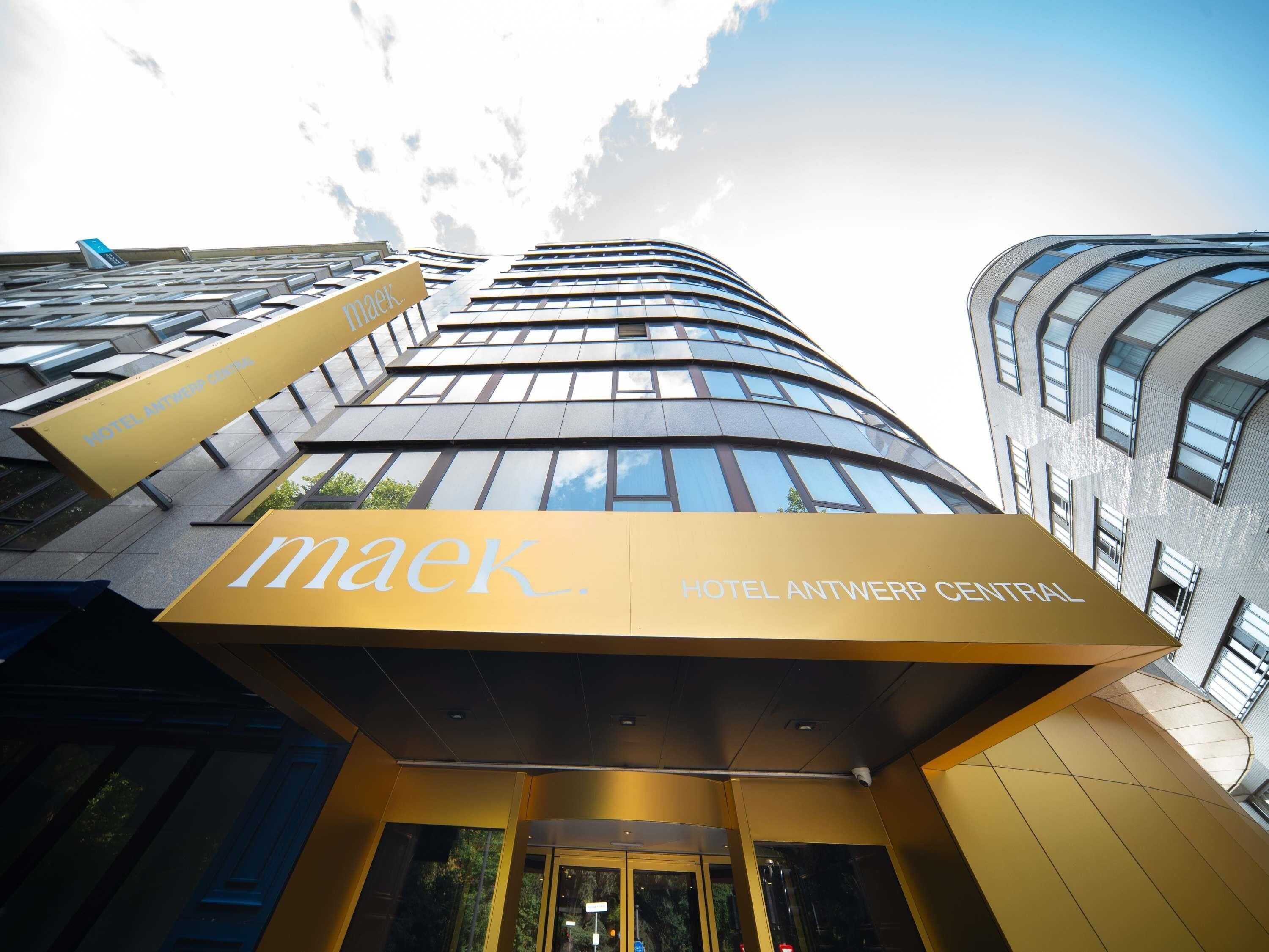 Exterior del Hotel Antwerp Central, con un diseño moderno, que presenta un llamativo letrero 'maek' y una fachada curva.