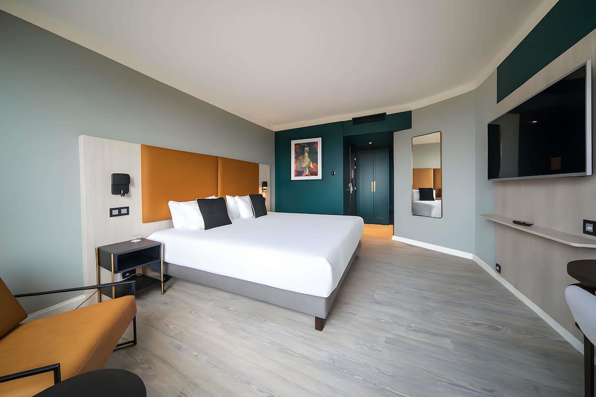 A modern hotel room with a large bed, a TV, a desk, and a chair.