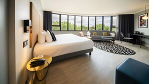 A modern hotel room with a large bed, a desk, a sofa, and a view of trees through large windows. - Maek Hotel Antwerp Central - Handwritten Collection (Antwerp)