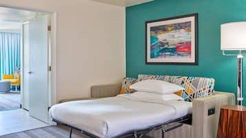 A hotel room with a bed, a teal accent wall, a framed abstract painting, and a bedside lamp.